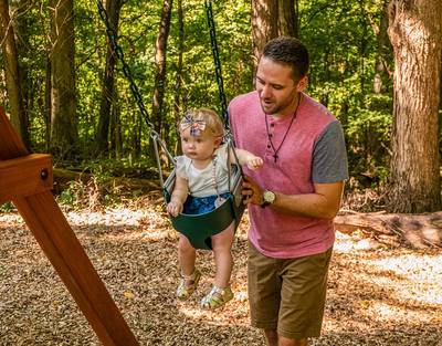 Man pushing little girl in green Woodplay bucket swing